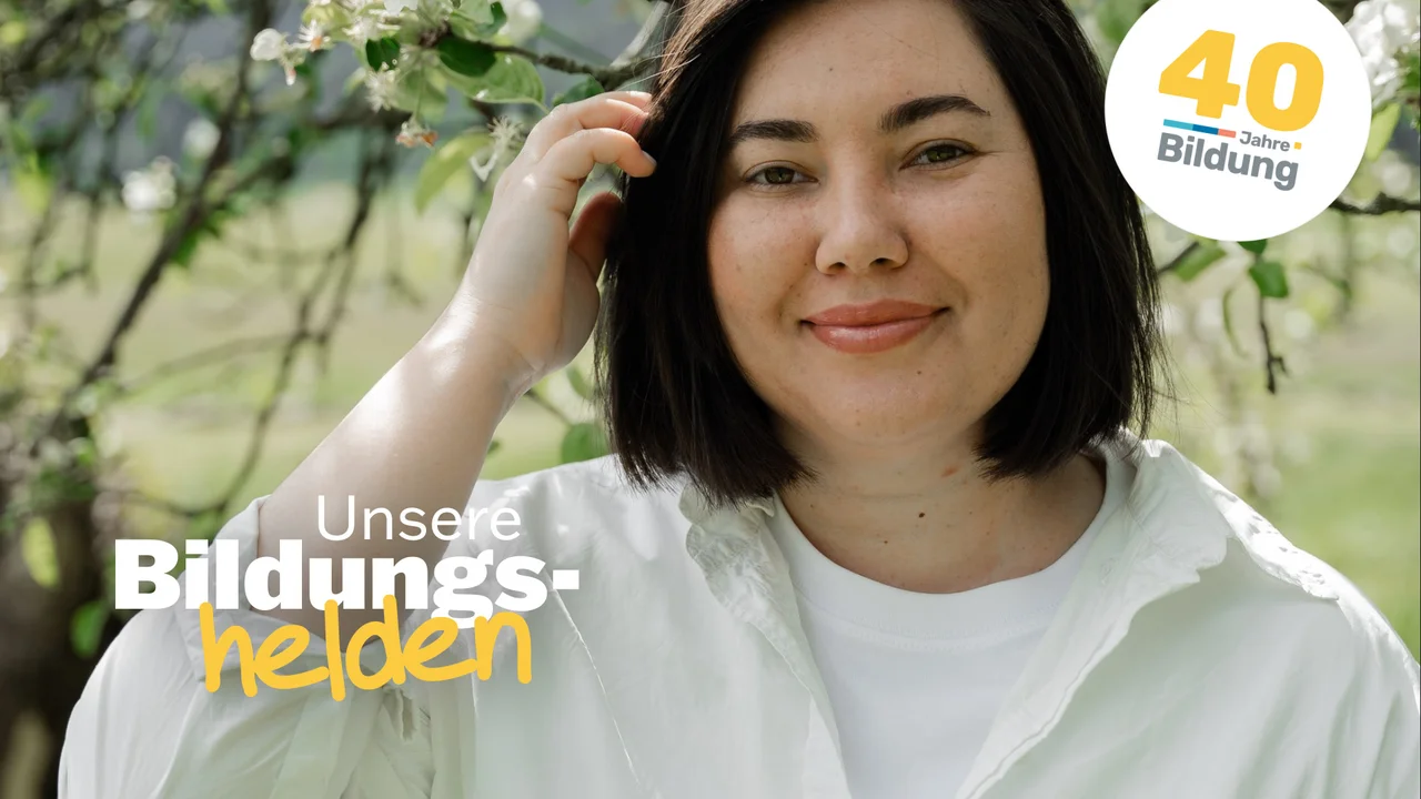 Video-Vorschaubild aus der Reihe "40 Jahre IBB - Bildungshelden": IBB-Dozentin Anzhelika Zavhorodnia steht draußen in der Sonne vor einem blühenden Obstbaum und streicht sich die Haare zurück.