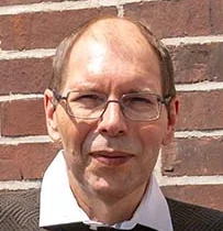 Der erfolgreiche Umschüler André Pardun steht mit verschränkten Armen vor einer geziegelten Hauswand.