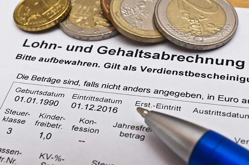 einen Stift und einige Münzen auf einem Papier mit der Aufschrift "Lohn- und Gehaltsabrechnung"